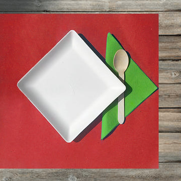 Apparecchiatura su tavolo di legno con tovaglietta rossa, tovagliolo verde, piatto bianco quadrato e cucchiaio in legno